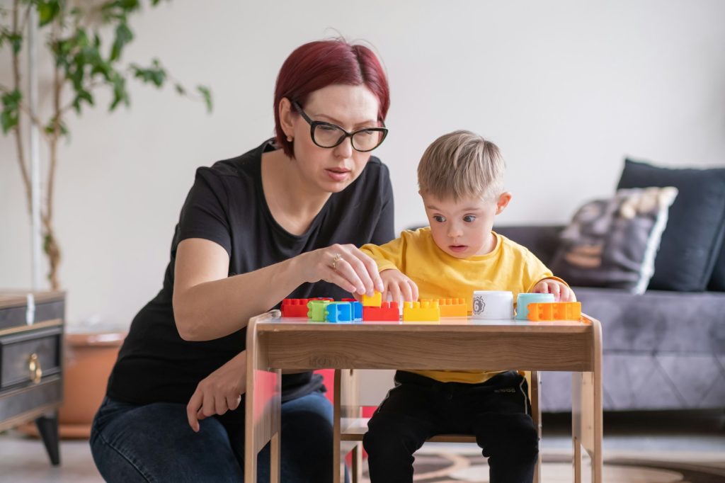 child living with Down syndrome learning and playing with educational toys, supported by his mom