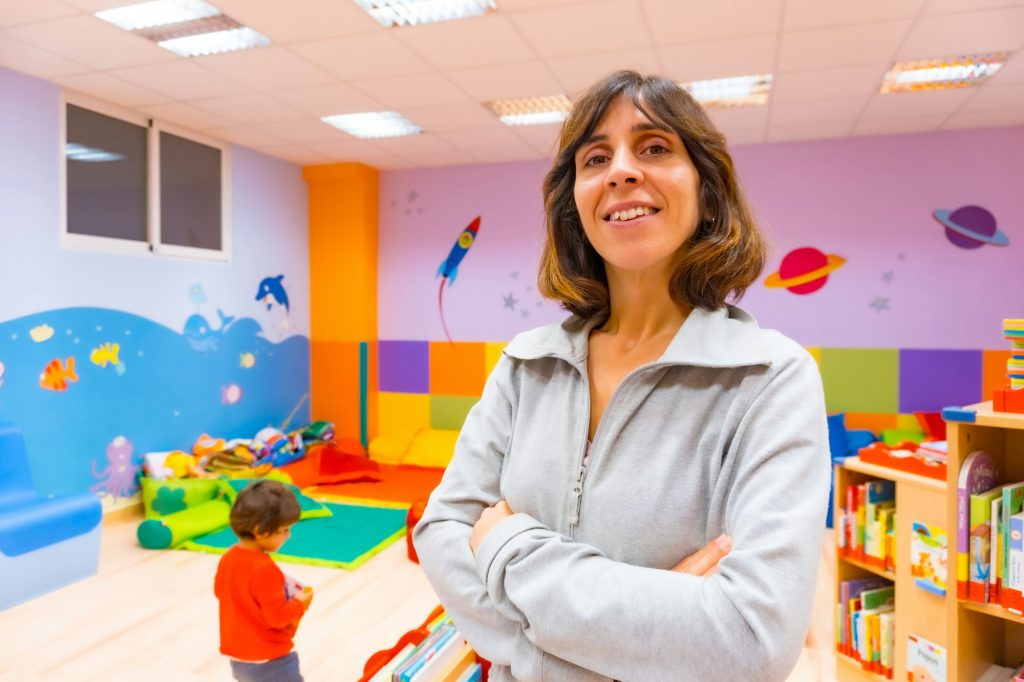 Portrait of a kindergarten or early childhood education teacher inside a kindergarten, with a child