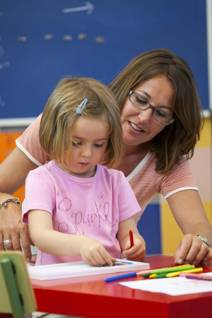 Preschool girl and teacher with colouring pens in classroom