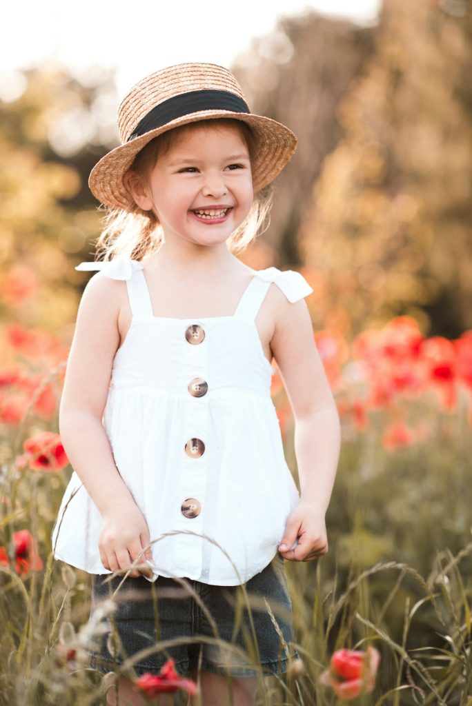 Smiling happy child girl 3-4 year old holding flower stand in poppy meadow outdoors